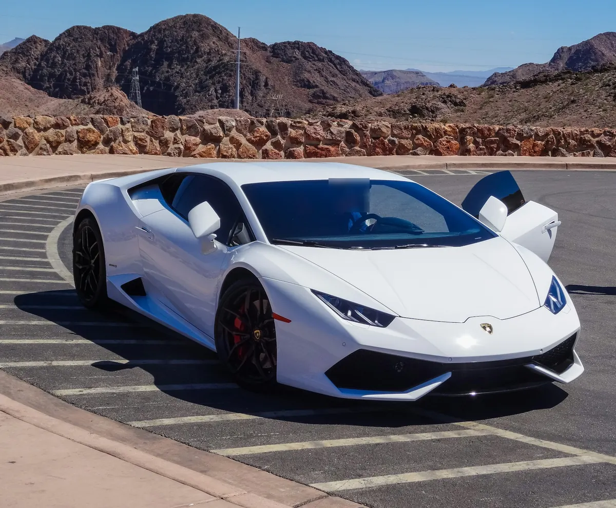 Front three-quarter view of a white Lamborghini Huracán LP 610-4 with a door open in a desert parking lot