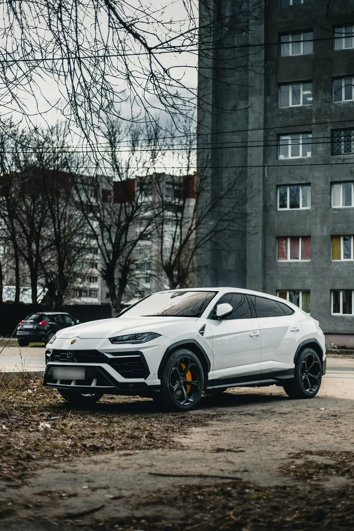 Front three-quarter view of a white Lamborghini Urus parked beside apartment buildings