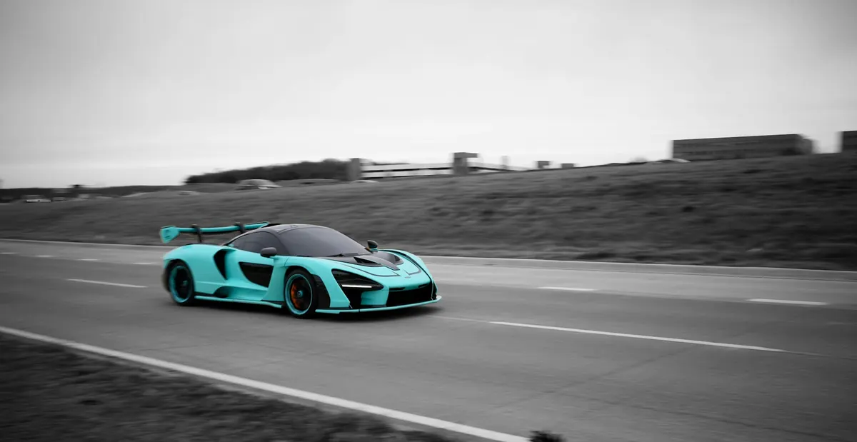 Front three-quarter view of a teal McLaren Senna driving on a road