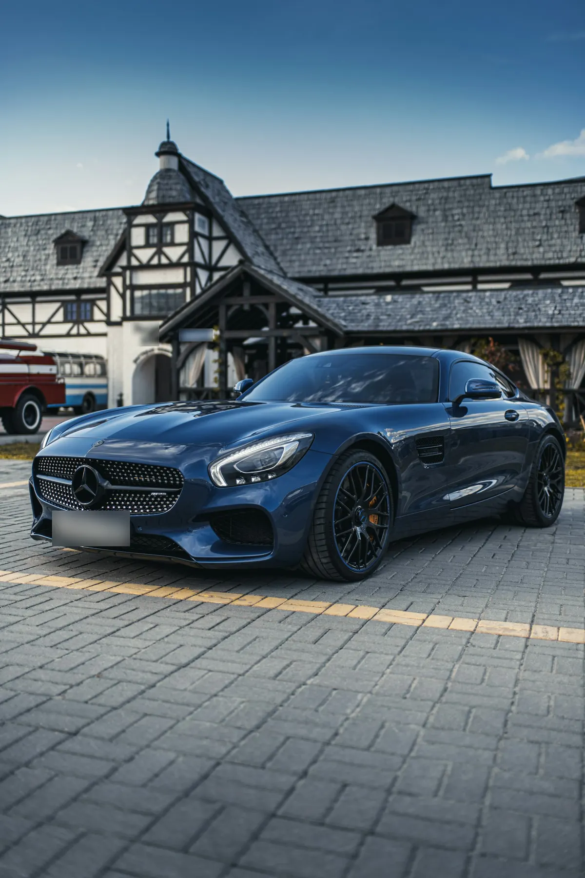 Front three-quarter view of a dark blue Mercedes-AMG GT (C190) coupe outside a timber-framed building