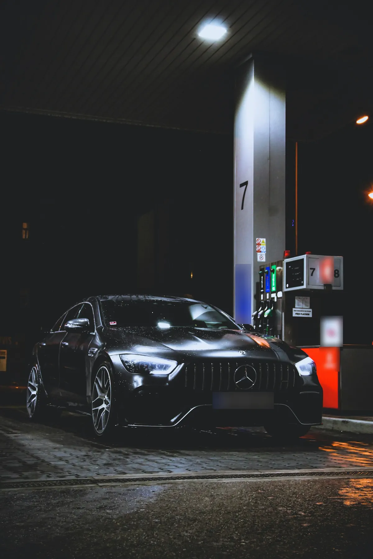 Front three-quarter view of a black Mercedes-AMG GT 63 4-Door Coupé (X290) at a fuel station at night