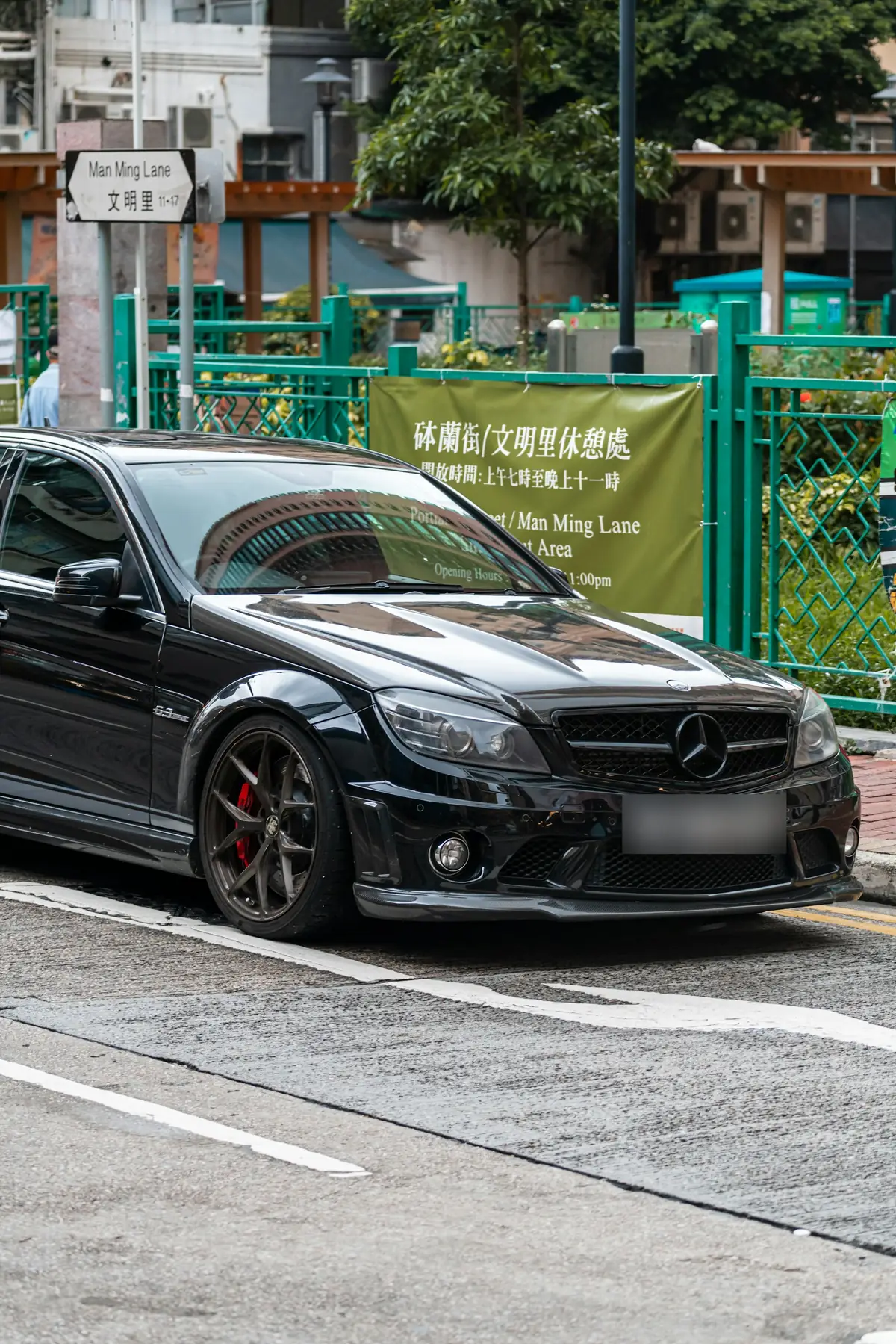 Front three-quarter view of a black Mercedes-AMG C63 (W204) sedan parked on a street in Hong Kong