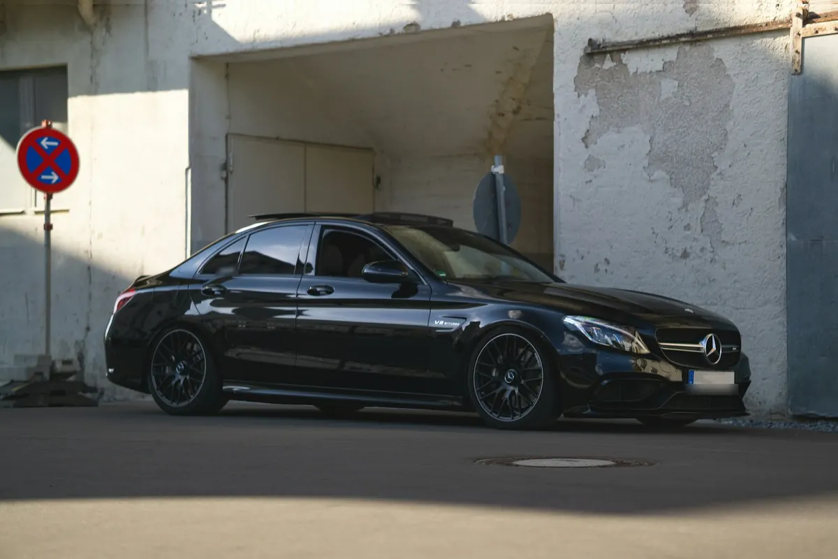 Front three-quarter view of a black Mercedes-AMG C63 (W205) sedan in front of a white wall