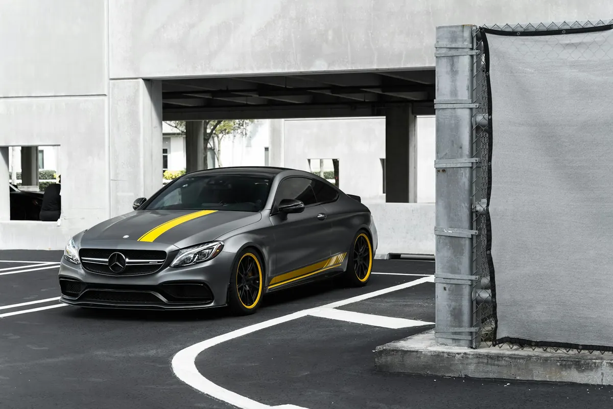 Front three-quarter view of a matte grey Mercedes-AMG C63 S (W205) coupe with yellow stripes in a parking lot