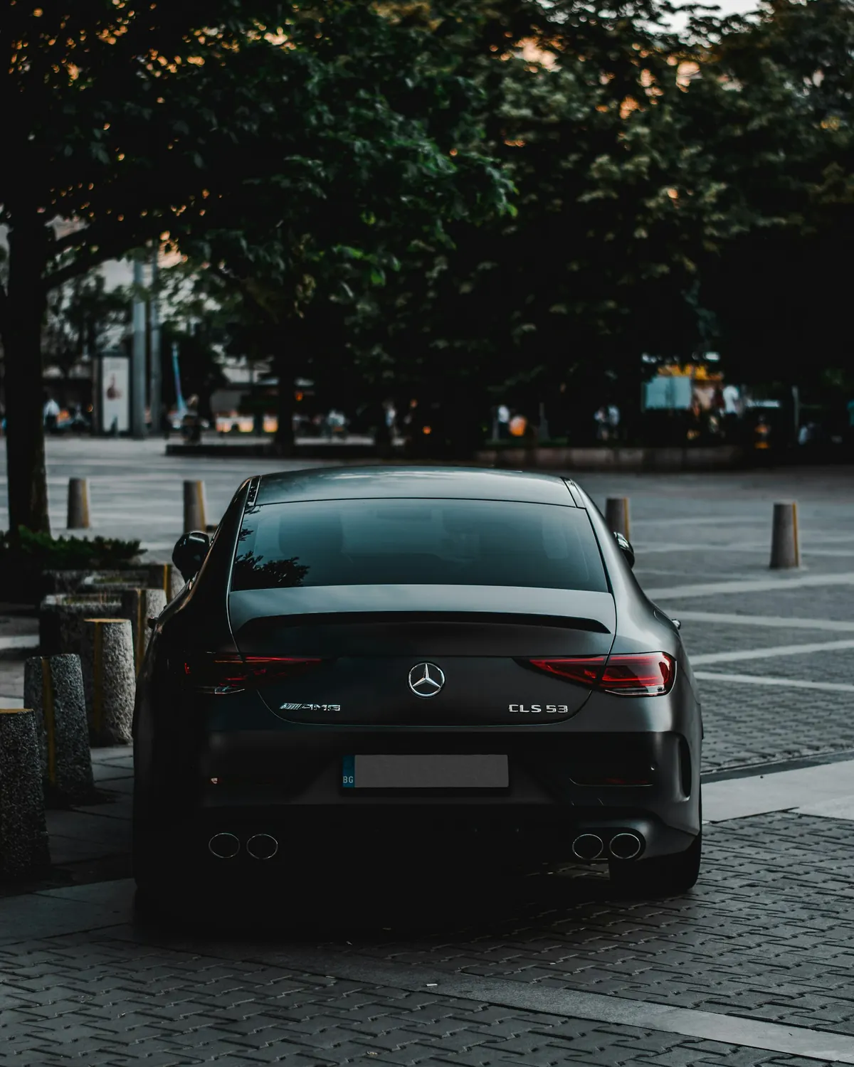 Rear view of a matte dark grey Mercedes-AMG CLS53 (C257) parked on a paved square at dusk