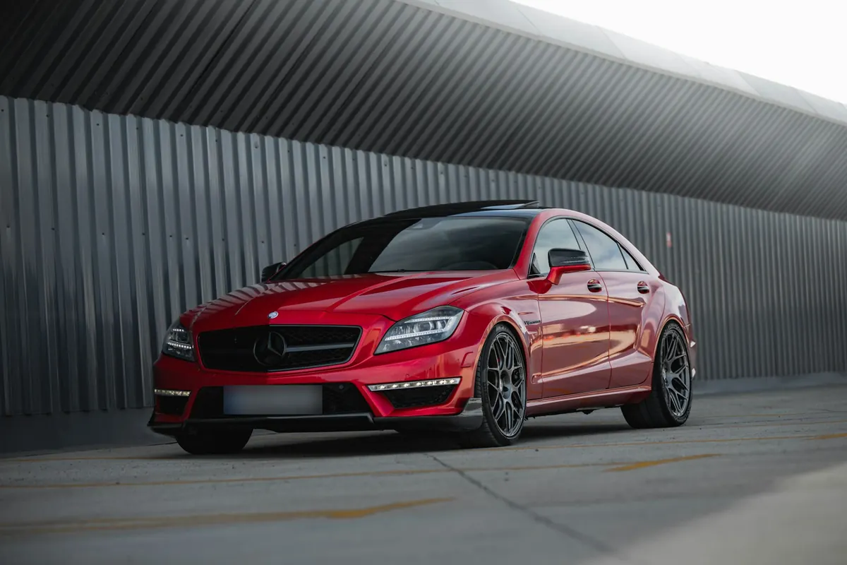 Front three-quarter view of a red Mercedes-AMG CLS63 S (C218) beside a corrugated metal wall