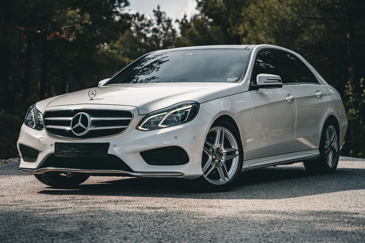 Front three-quarter view of a white Mercedes-Benz E550 (W212) sedan on a forest road