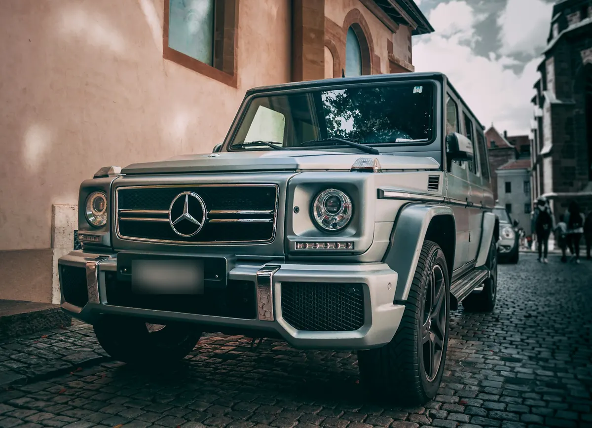 Front three-quarter view of a silver Mercedes-AMG G63 (W463) on a cobblestone street