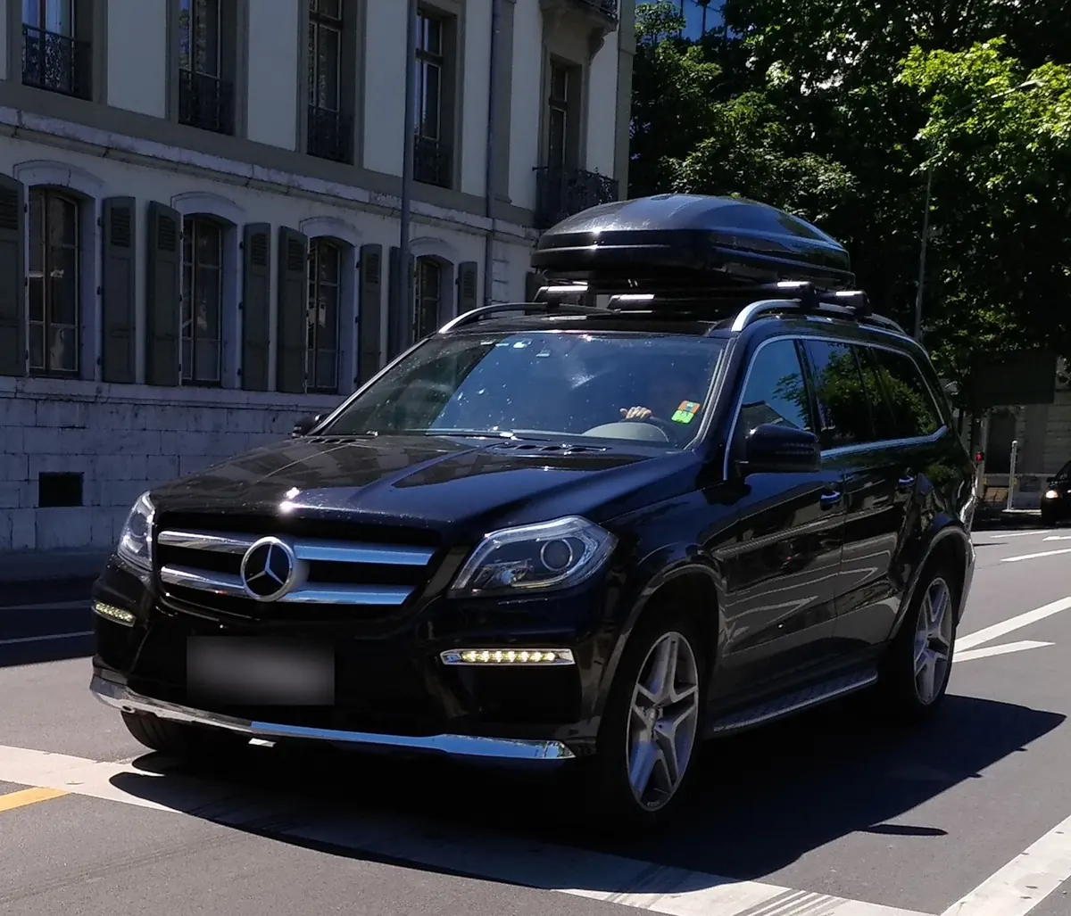 Front three-quarter view of a black Mercedes-Benz GL550 (X166) with a roof box on a city street