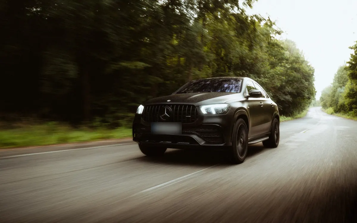 Front three-quarter view of a matte black Mercedes-AMG GLE53 Coupe (C167) driving on a forest road