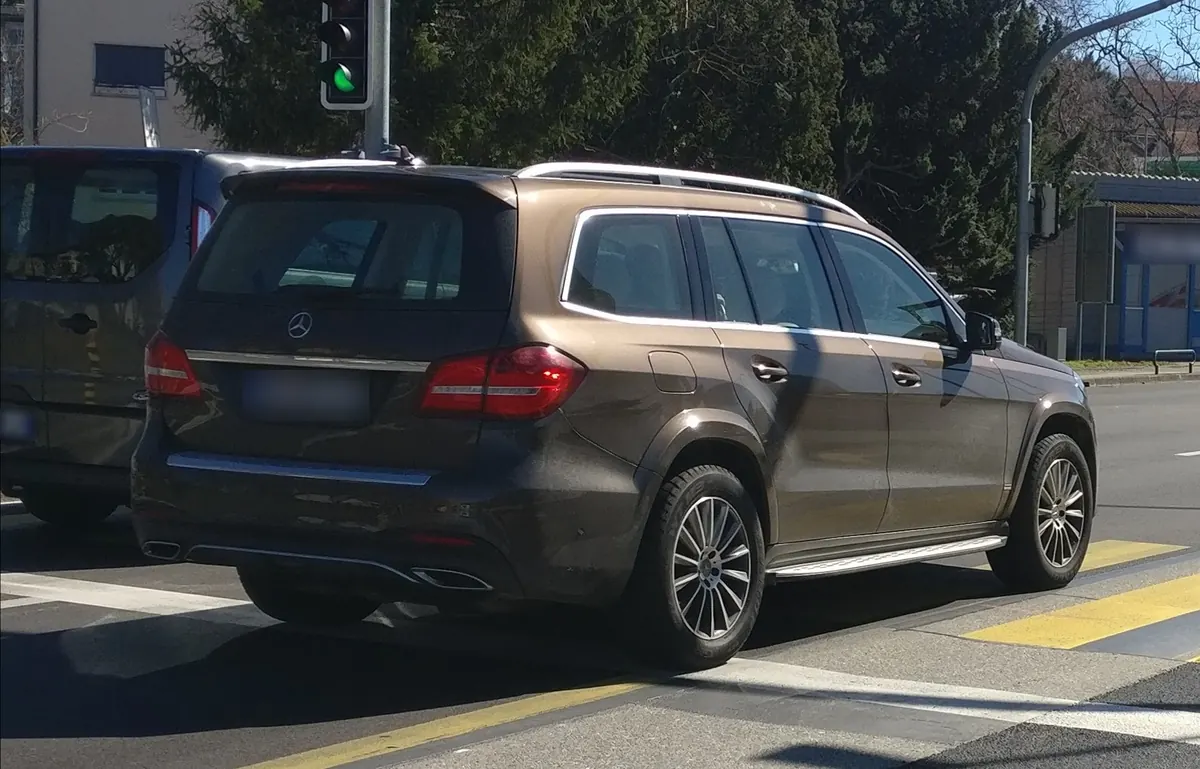 Rear three-quarter view of a brown Mercedes-Benz GLS550 (X166) at a city street crossing