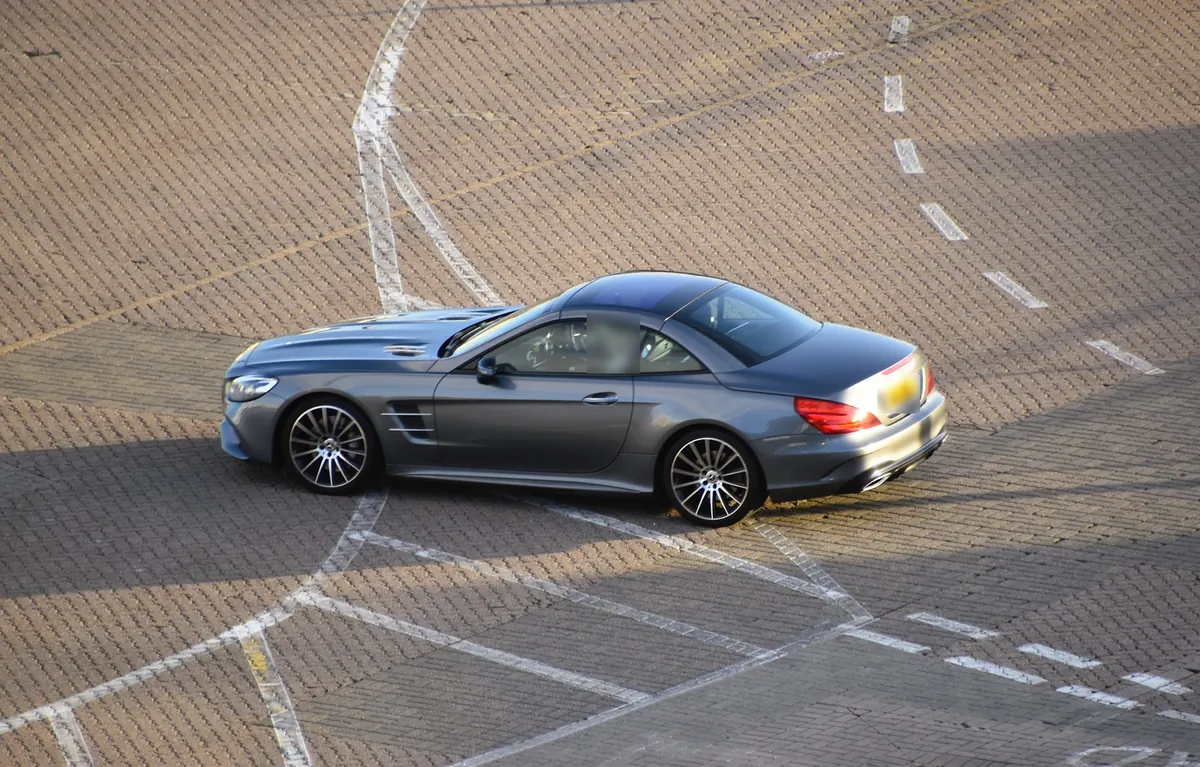 Side view from above of a grey Mercedes-Benz SL550 (R231) roadster with its hardtop closed on a paved lot