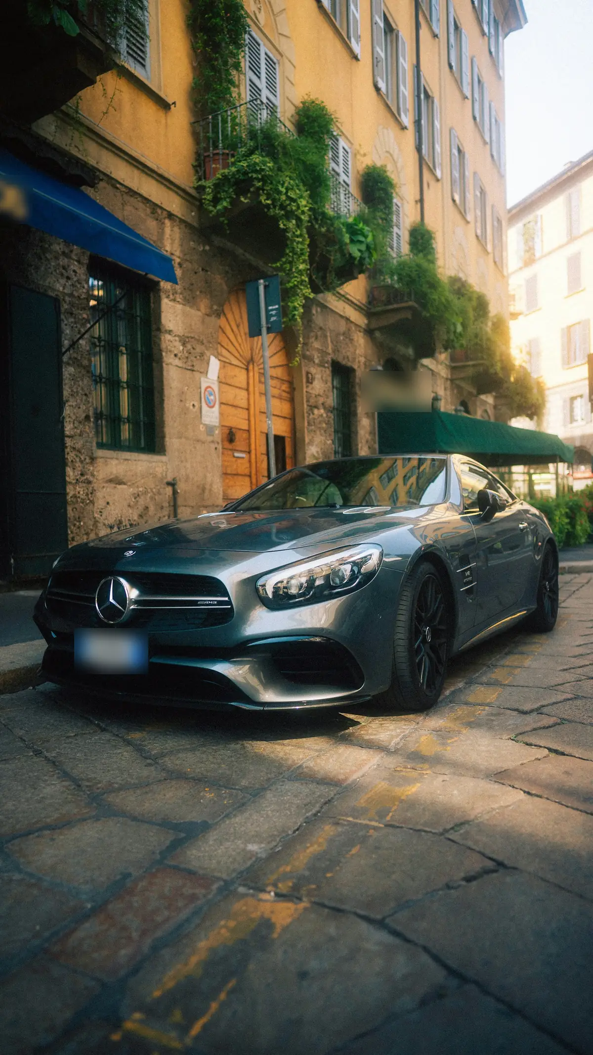 Front three-quarter view of a grey Mercedes-AMG SL63 (R231) with the roof up on a cobbled city street