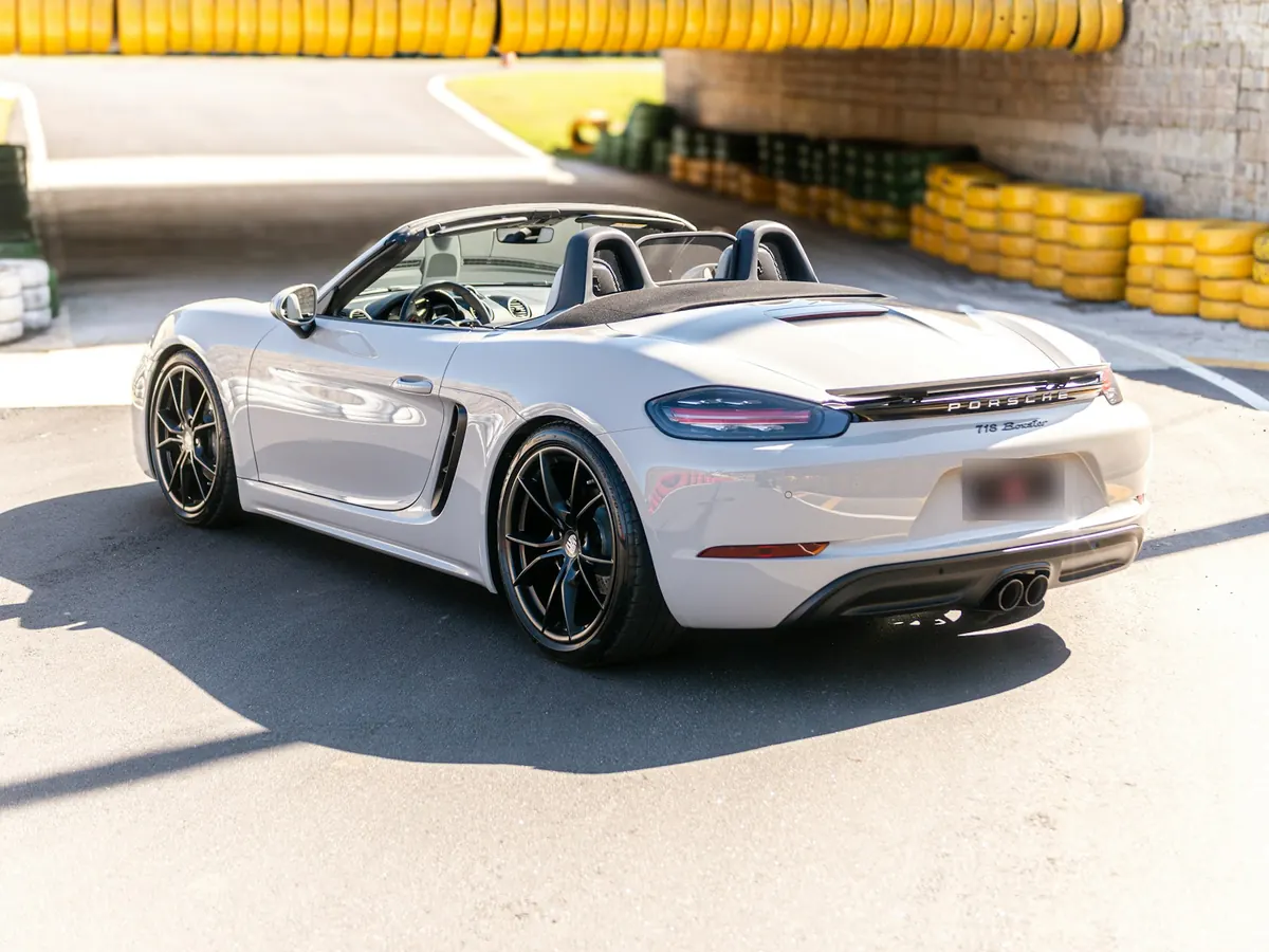 Rear three-quarter view of a light grey Porsche 718 Boxster (2.0) with the roof down at a race track