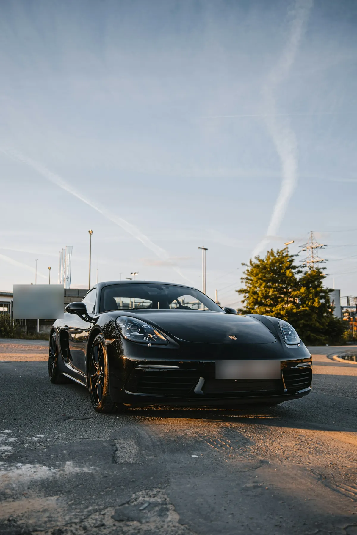 Front view of a black Porsche 718 Cayman S at sunset by an industrial site