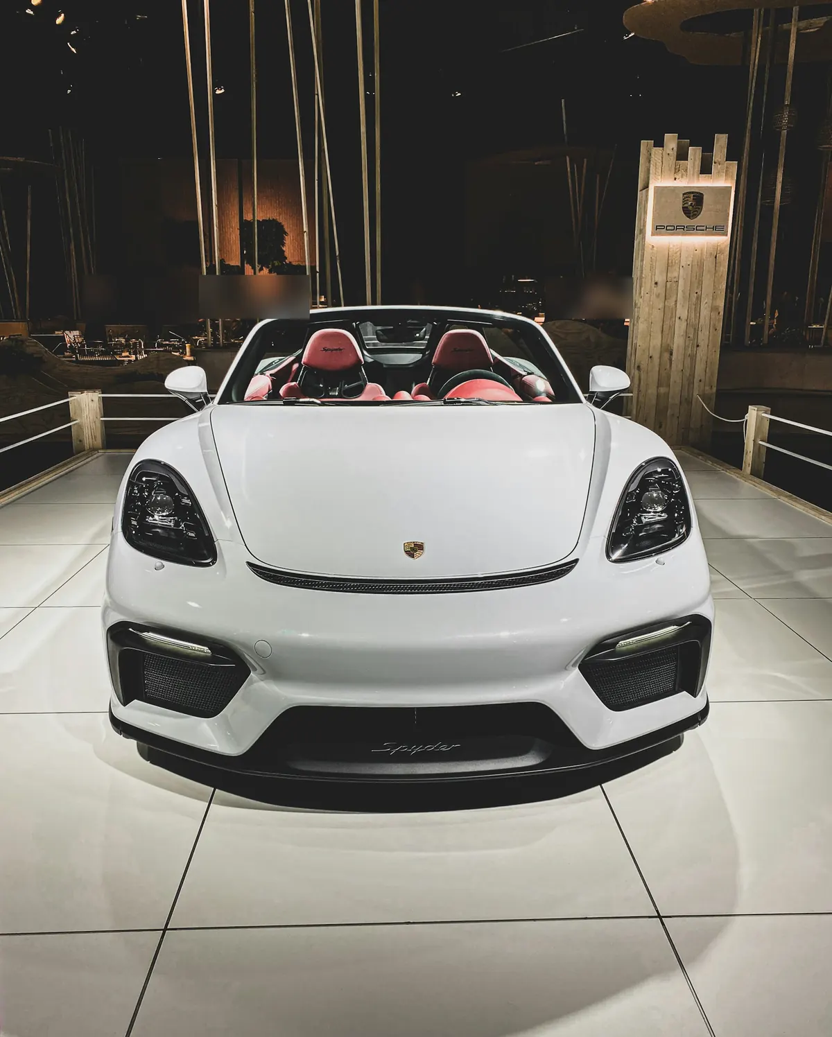 Front view of a white Porsche 718 Spyder with the roof down on an auto show stand