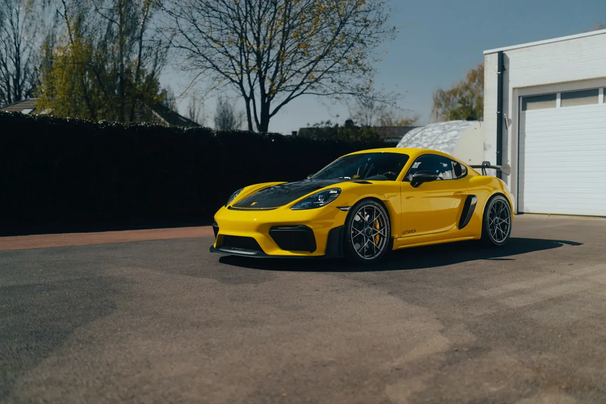 Front three-quarter view of a yellow Porsche 718 Cayman GT4 RS parked in front of a garage