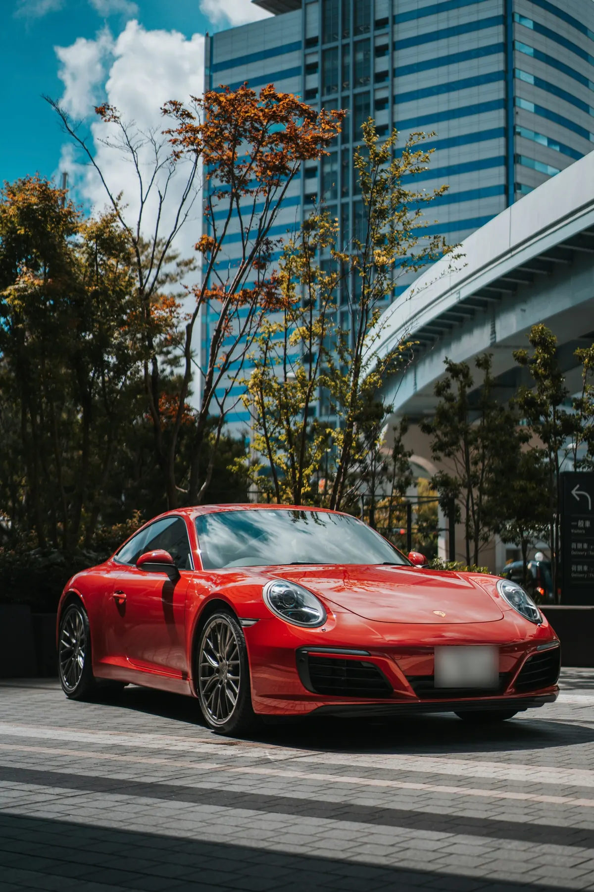 Front three-quarter view of a red Porsche 911 Carrera (991.2) parked in a city plaza