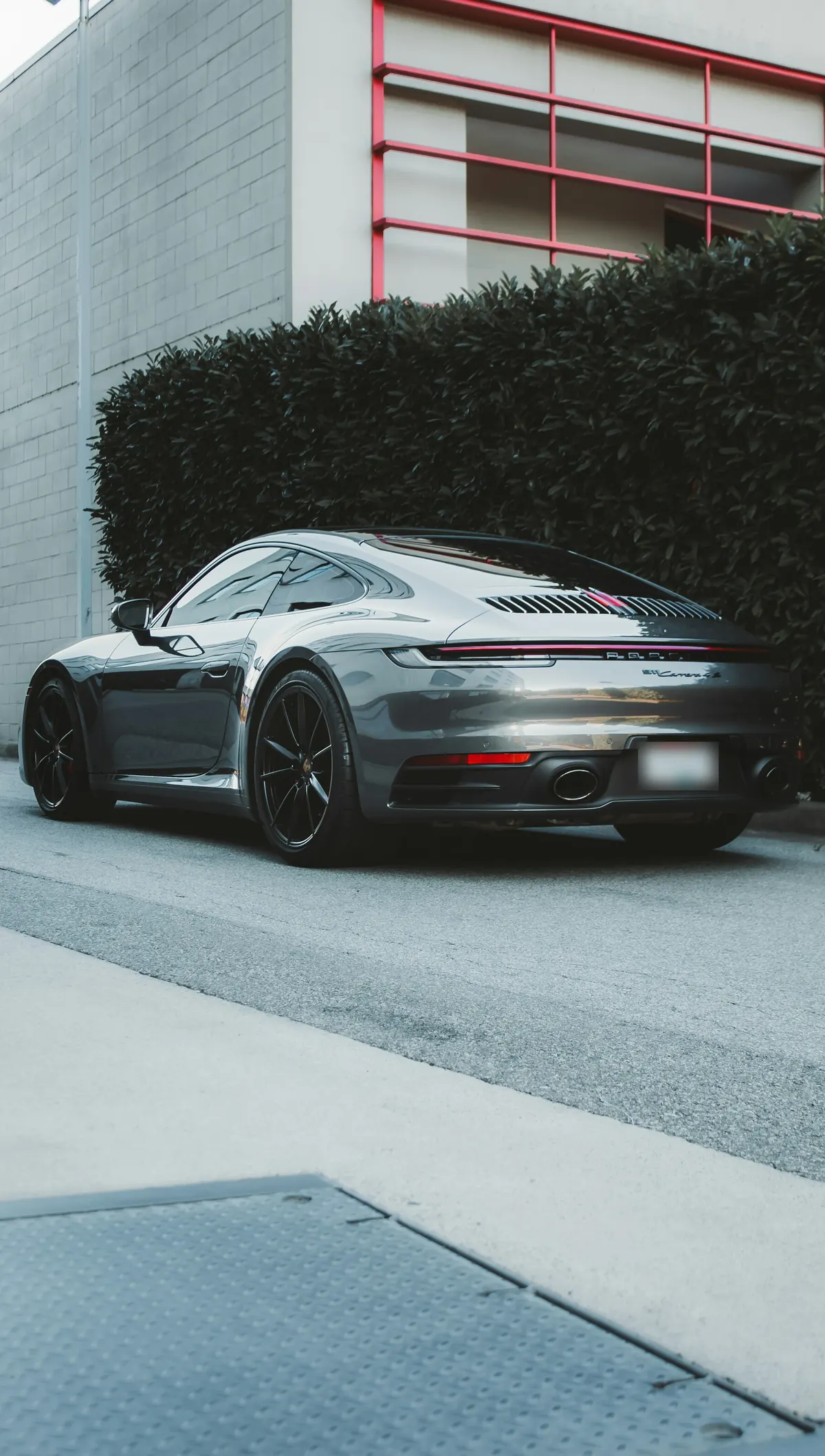 Rear three-quarter view of a grey Porsche 911 Carrera 4S (992.1) parked by a hedge