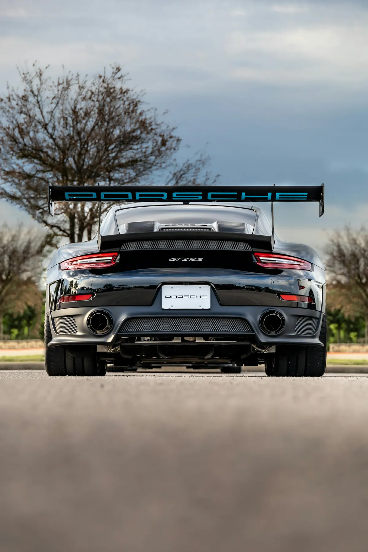 Rear view of a dark grey Porsche 911 GT2 RS (991.2) with its rear wing, on a road
