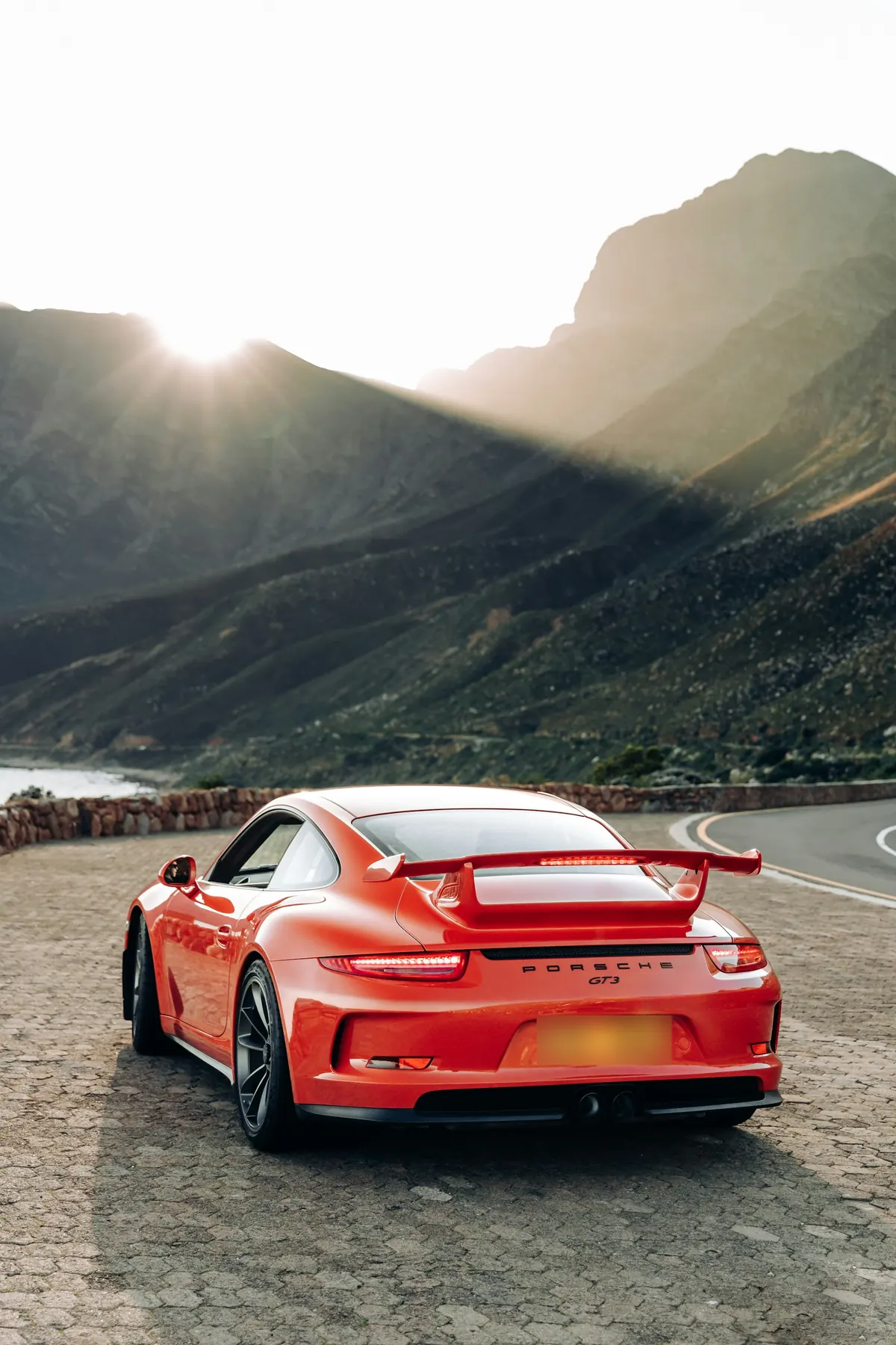 Rear three-quarter view of an orange Porsche 911 GT3 (991.1) on a mountain road