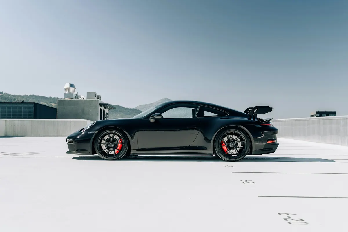 Side view of a black Porsche 911 GT3 (992.1) with red brake calipers on a rooftop parking lot