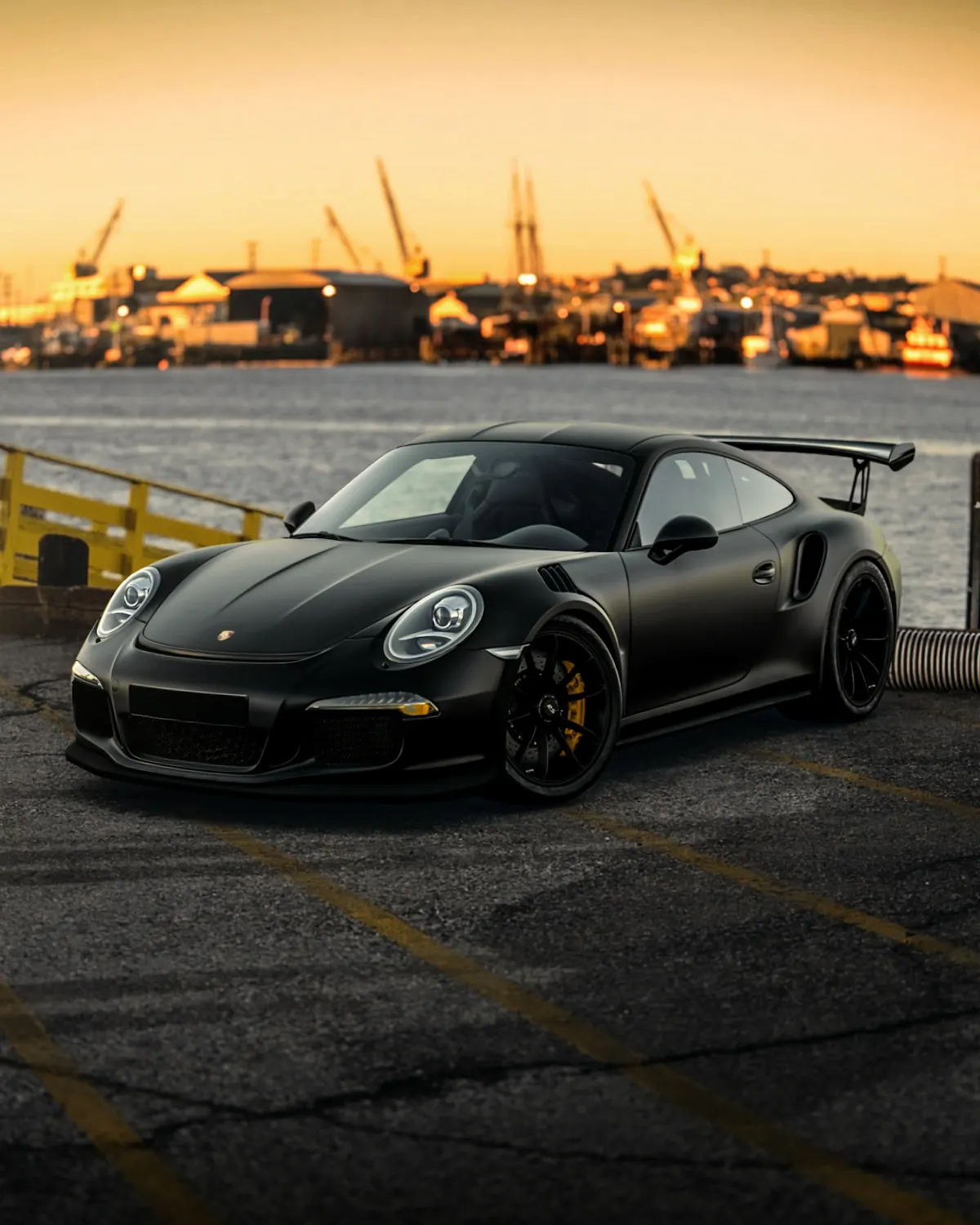 Front three-quarter view of a black Porsche 911 GT3 RS (991.1) on a harbor waterfront at sunset