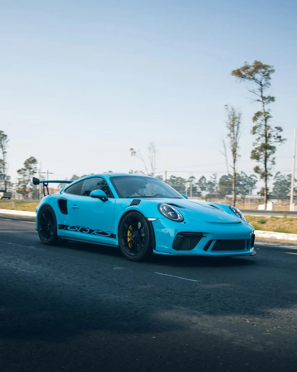 Front three-quarter view of a light blue Porsche 911 GT3 RS (991.2) driving on a road