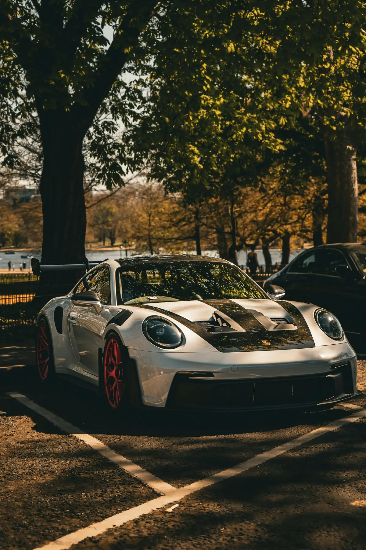 Front three-quarter view of a white Porsche 911 GT3 RS (992.1) with red wheels, parked under trees