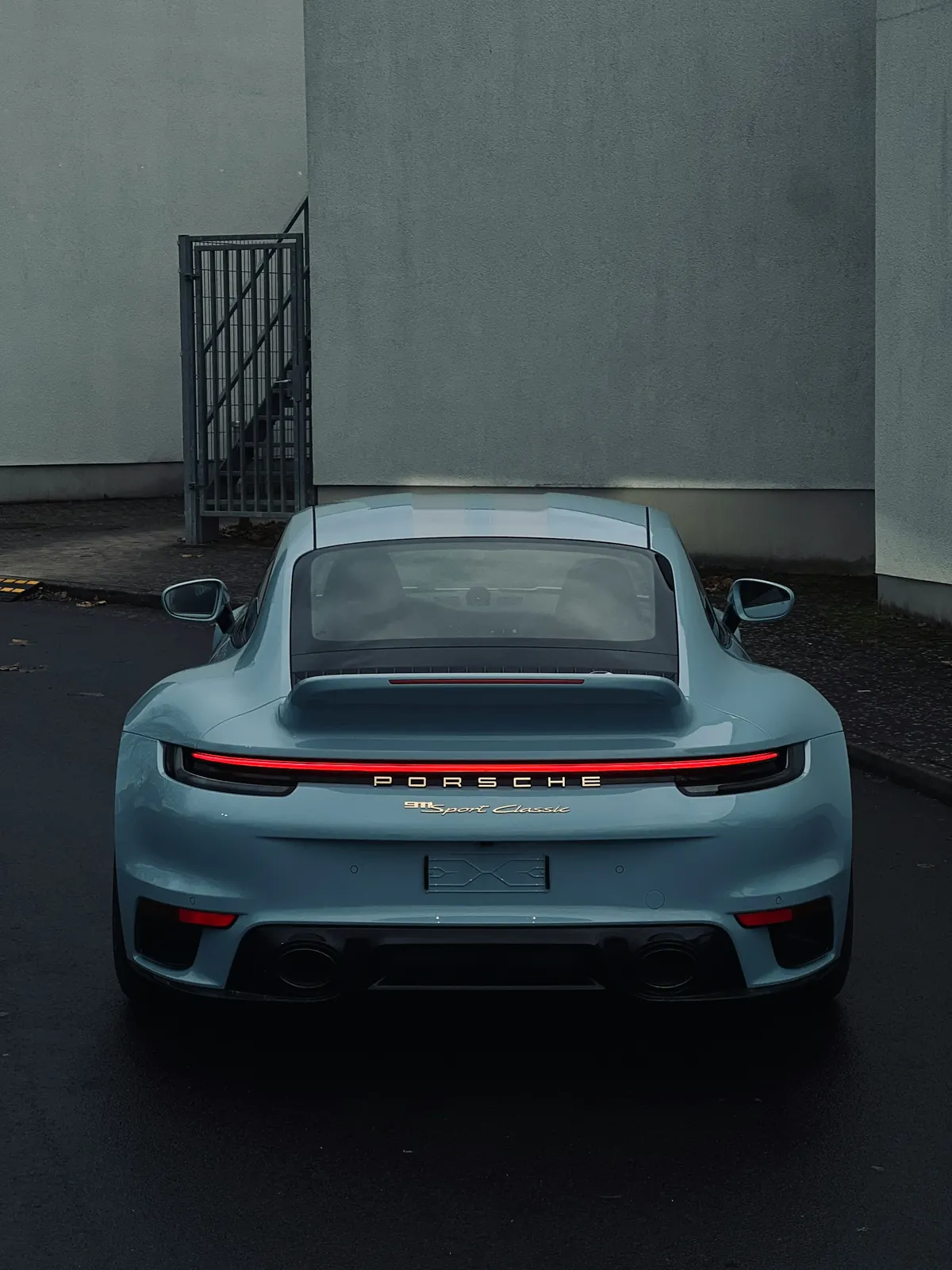 Rear view of a grey Porsche 911 Sport Classic (992.1) with its ducktail spoiler, parked by a building