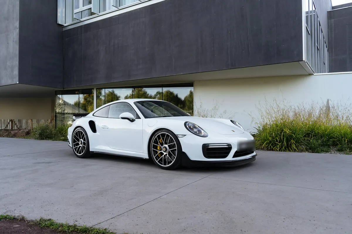 Front three-quarter view of a white Porsche 911 Turbo S (991.2) parked in front of a modern building