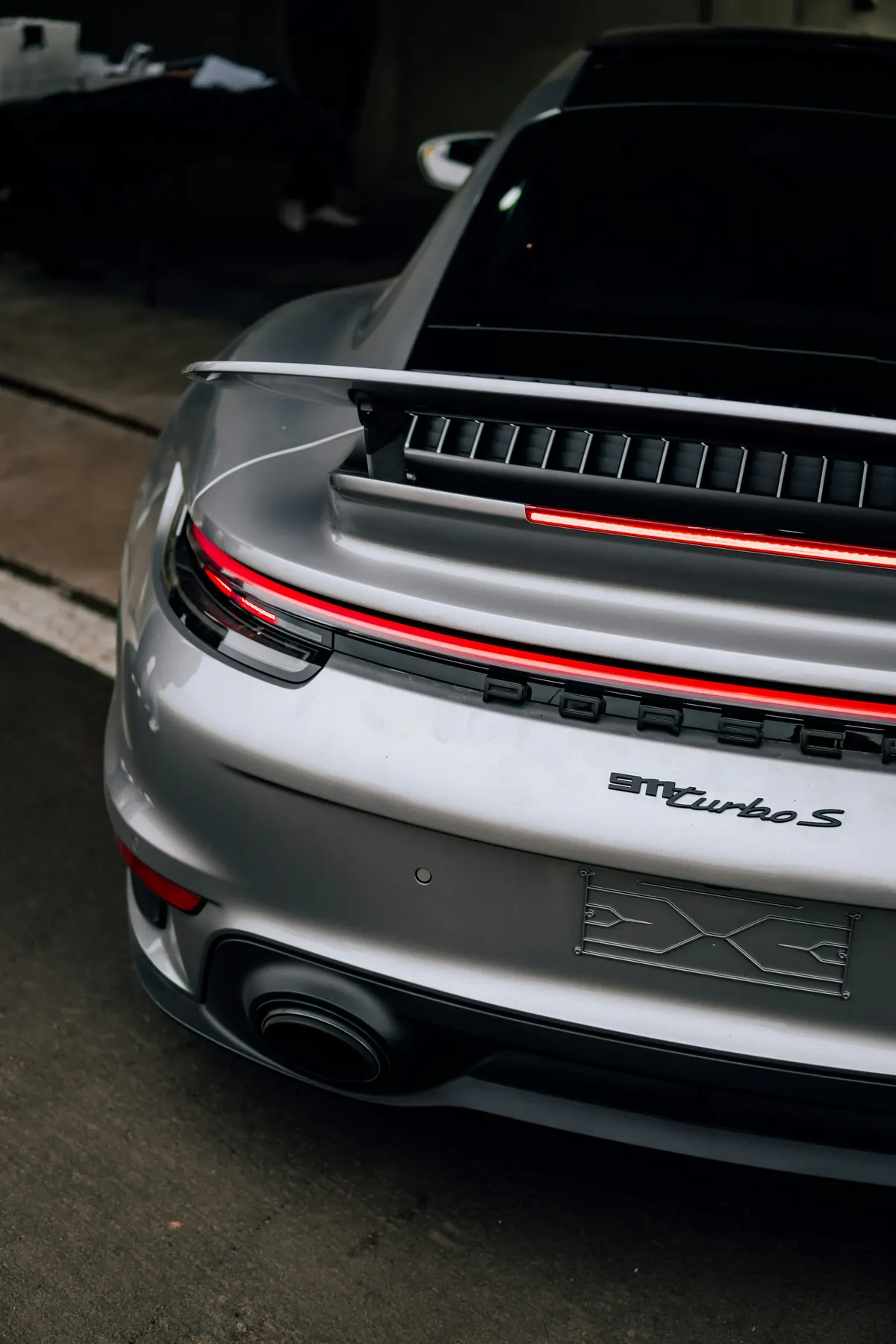 Close-up rear three-quarter view of a silver Porsche 911 Turbo S (992.1) with its rear wing raised
