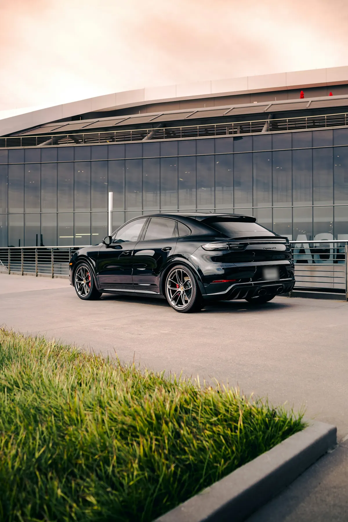 Rear three-quarter view of a black Porsche Cayenne GTS Coupe (E3.1) outside a glass building