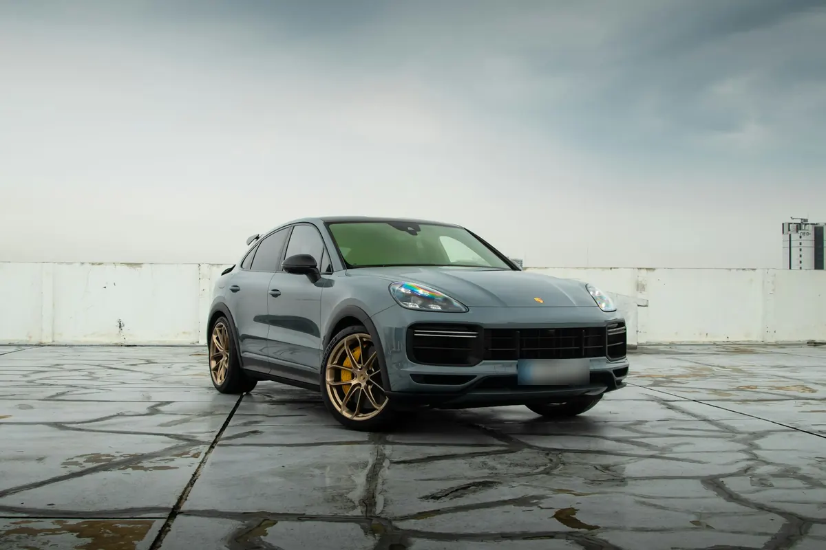 Front three-quarter view of a grey Porsche Cayenne Turbo GT (E3.1) with gold wheels on a rooftop parking lot