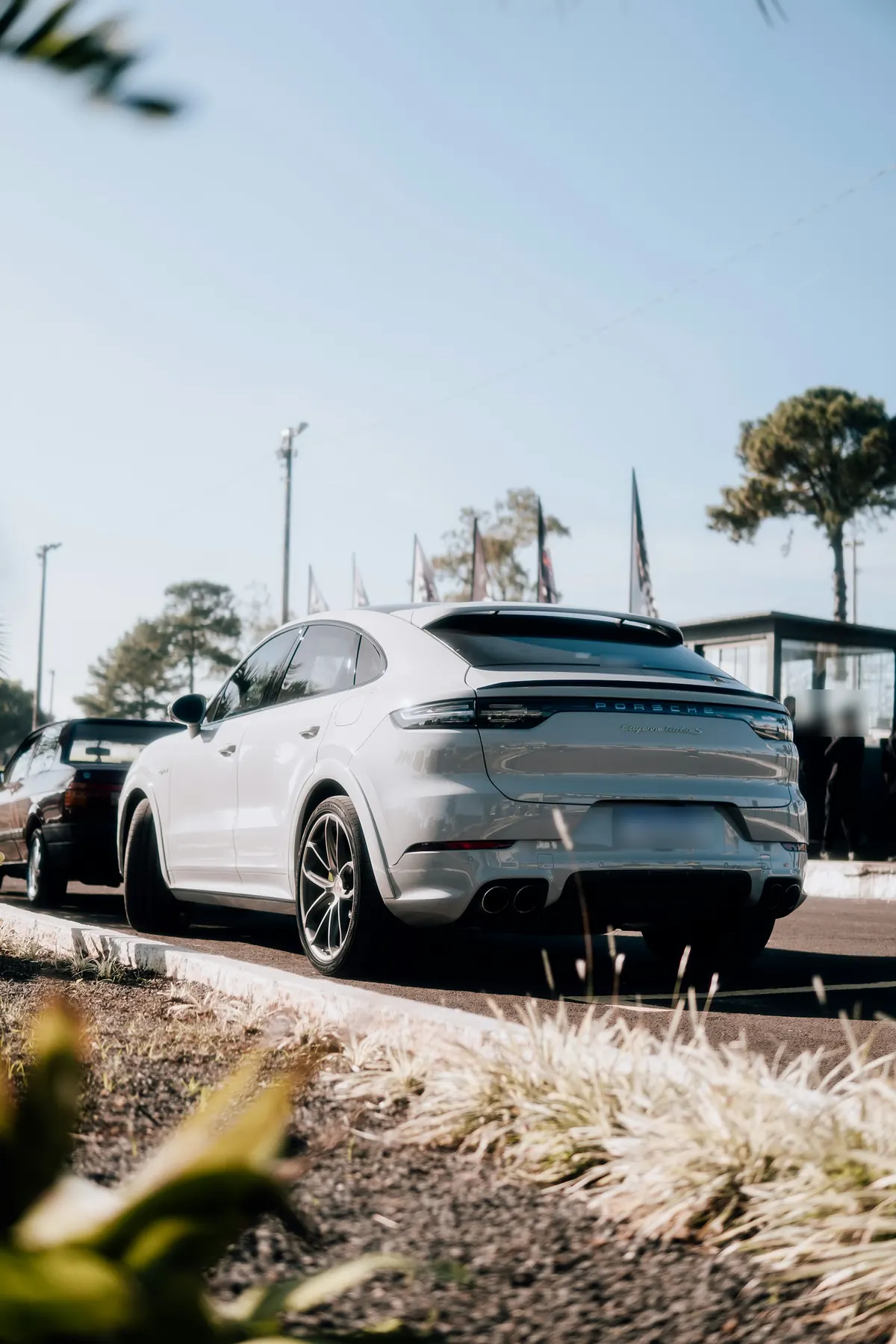 Rear three-quarter view of a light grey Porsche Cayenne Turbo S E-Hybrid Coupe (E3.1) at a racing event
