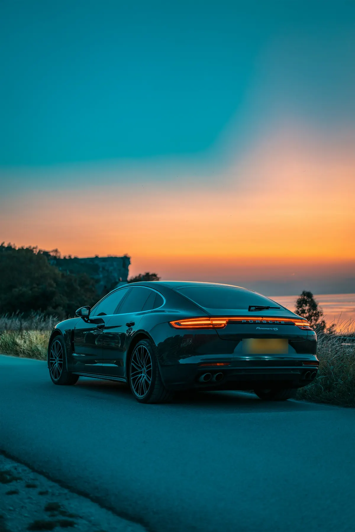 Rear three-quarter view of a dark blue Porsche Panamera 4S (971.1) on a coastal road at sunset