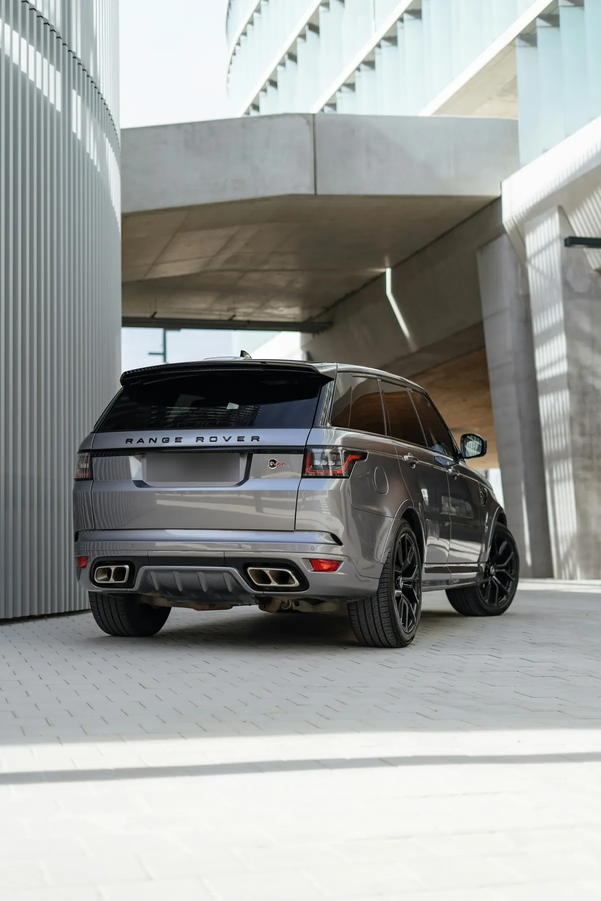 Rear three-quarter view of a grey Range Rover Sport SVR (L494) parked beneath a concrete building
