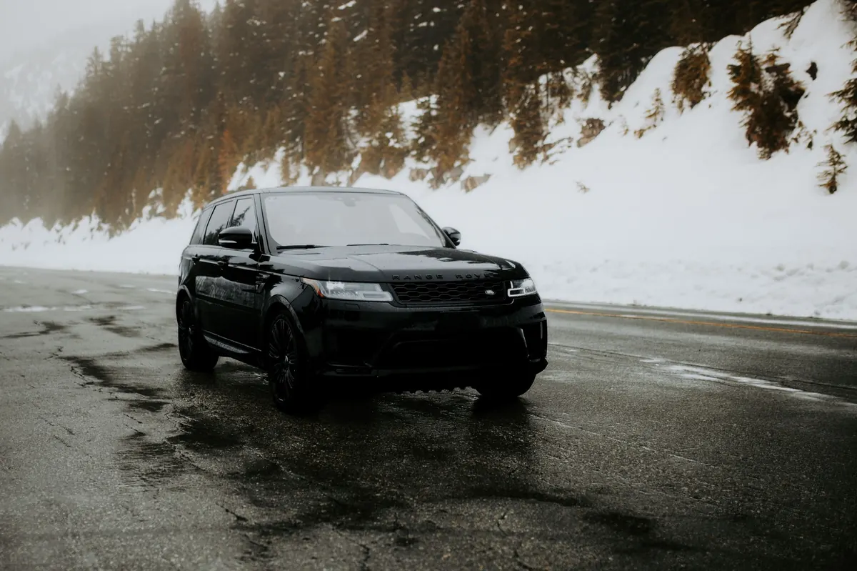 Front three-quarter view of a black Range Rover Sport V8 Supercharged (L494) on a wet mountain road in the snow