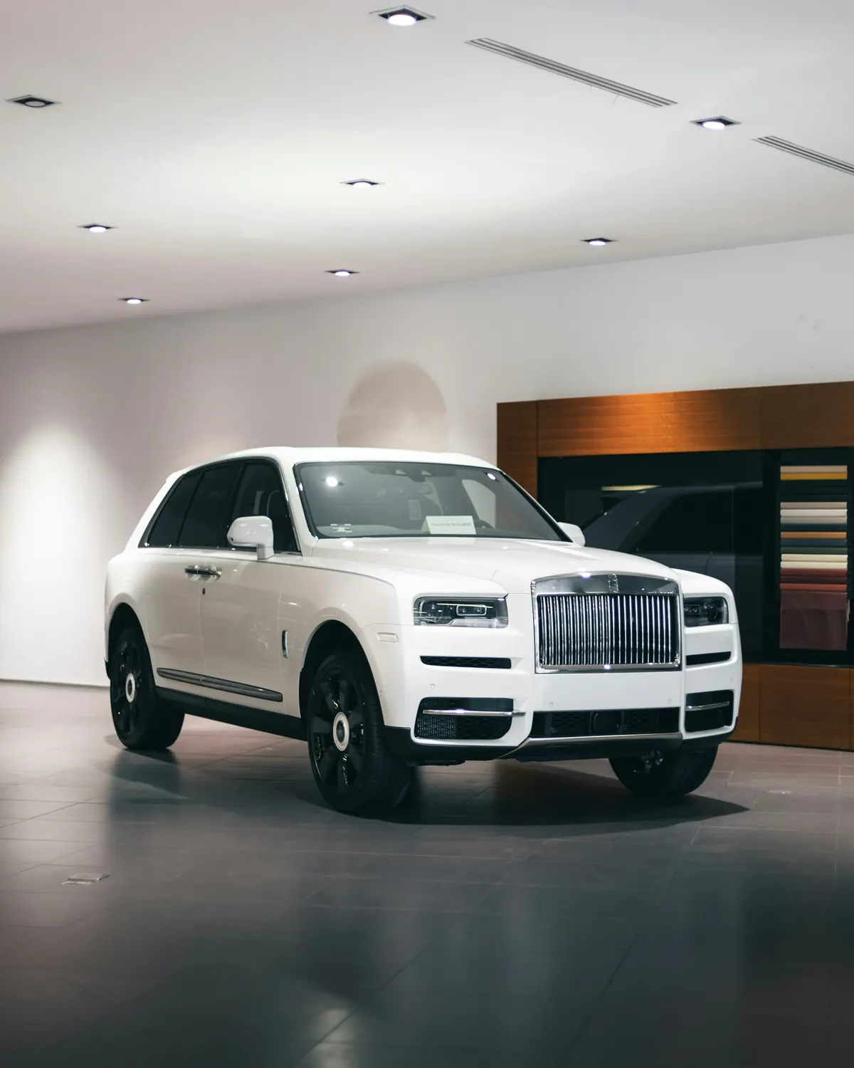Front three-quarter view of a white Rolls-Royce Cullinan with black wheels in a showroom