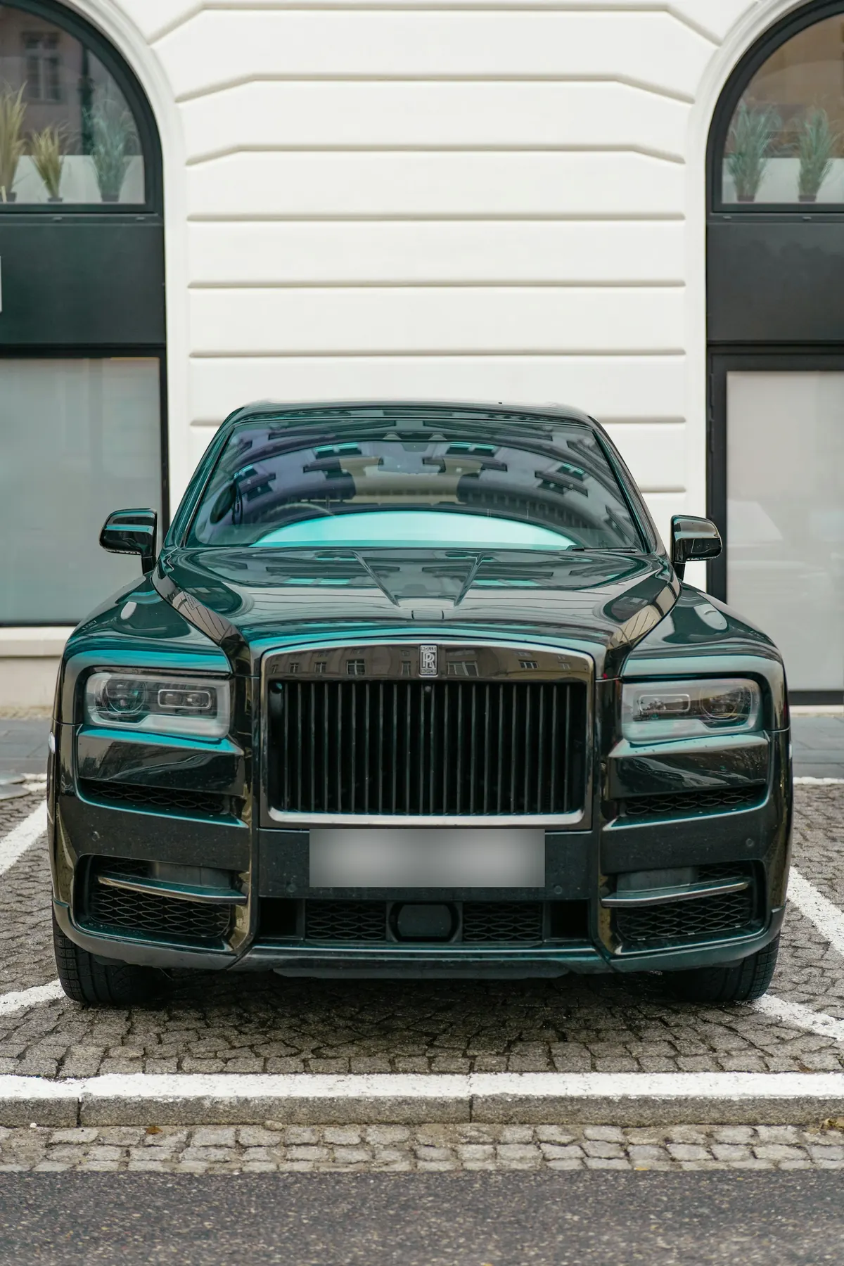 Front view of a dark green Rolls-Royce Cullinan Black Badge parked on cobblestones outside a white building