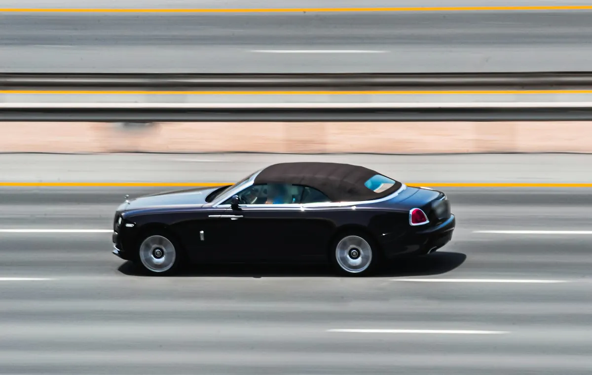 Side view of a black Rolls-Royce Dawn with its brown fabric roof up, driving on a highway