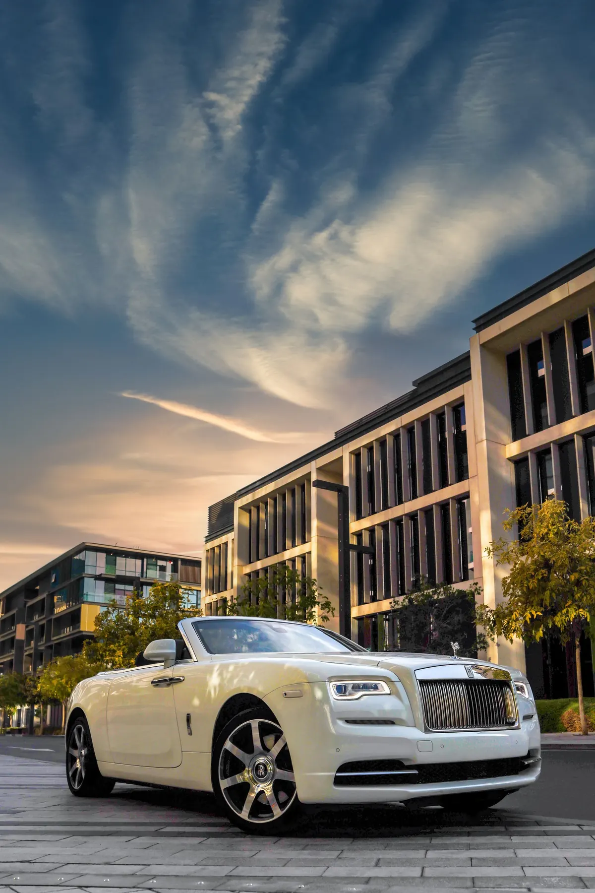 Front three-quarter view of a white Rolls-Royce Dawn Black Badge with the roof down outside modern buildings