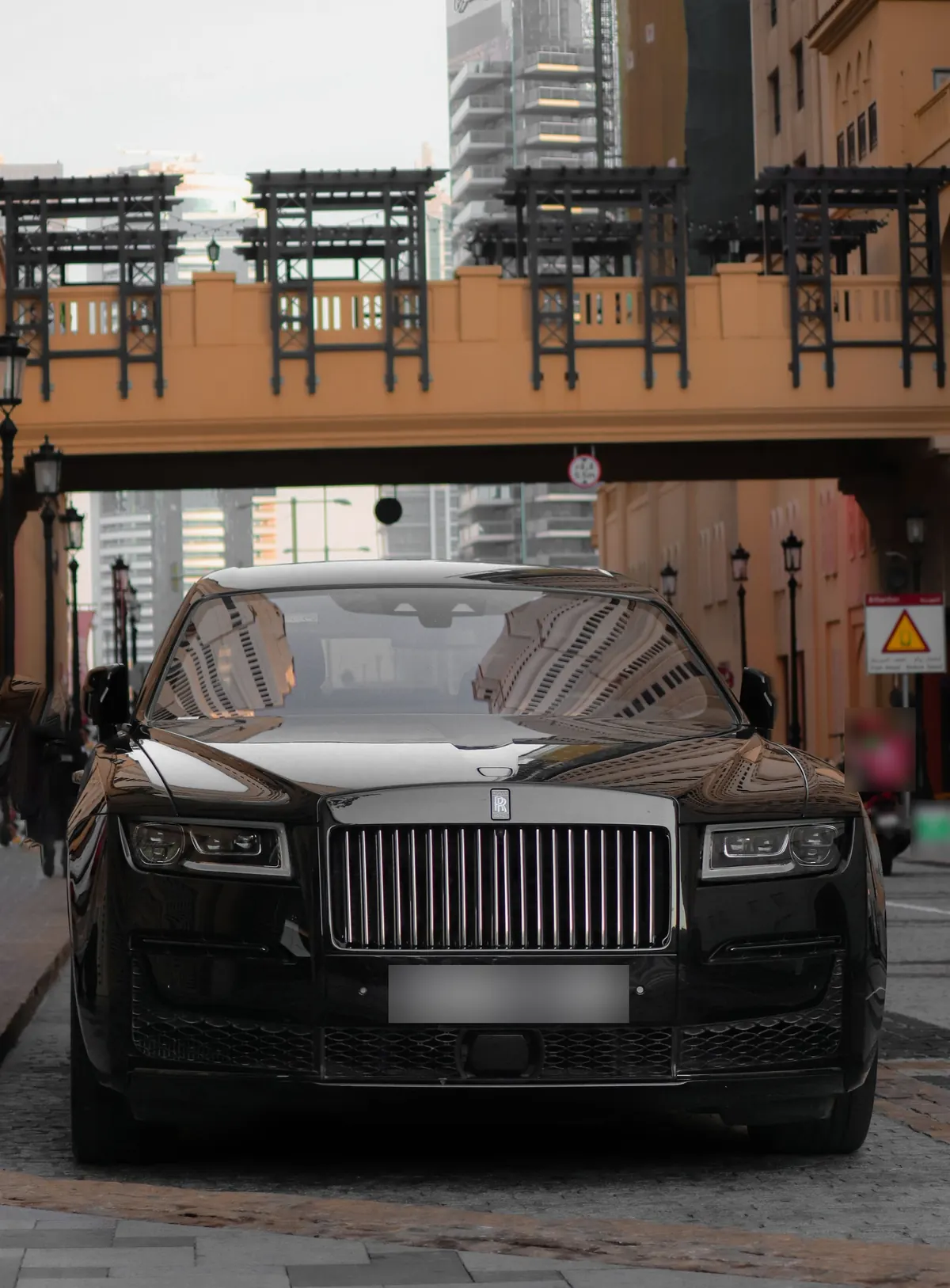 Front view of a black Rolls-Royce Ghost (second generation) on a city street beneath a footbridge