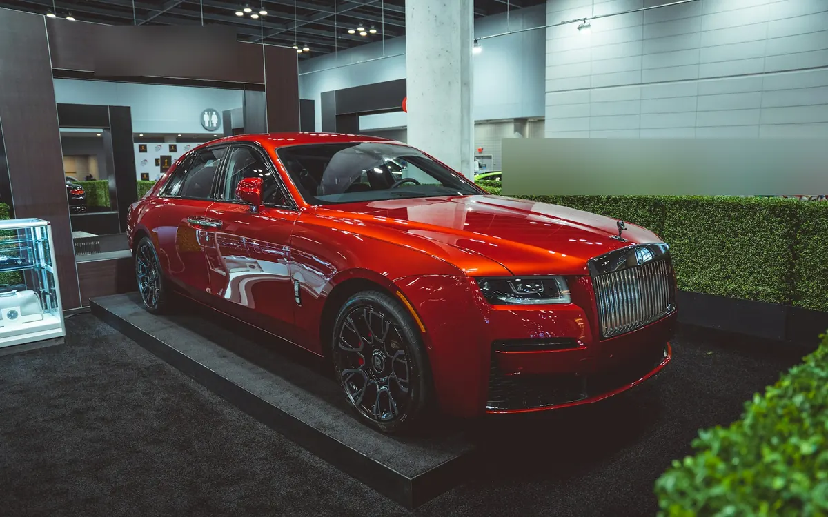 Front three-quarter view of a red Rolls-Royce Ghost Black Badge (second generation) on a motor show stand