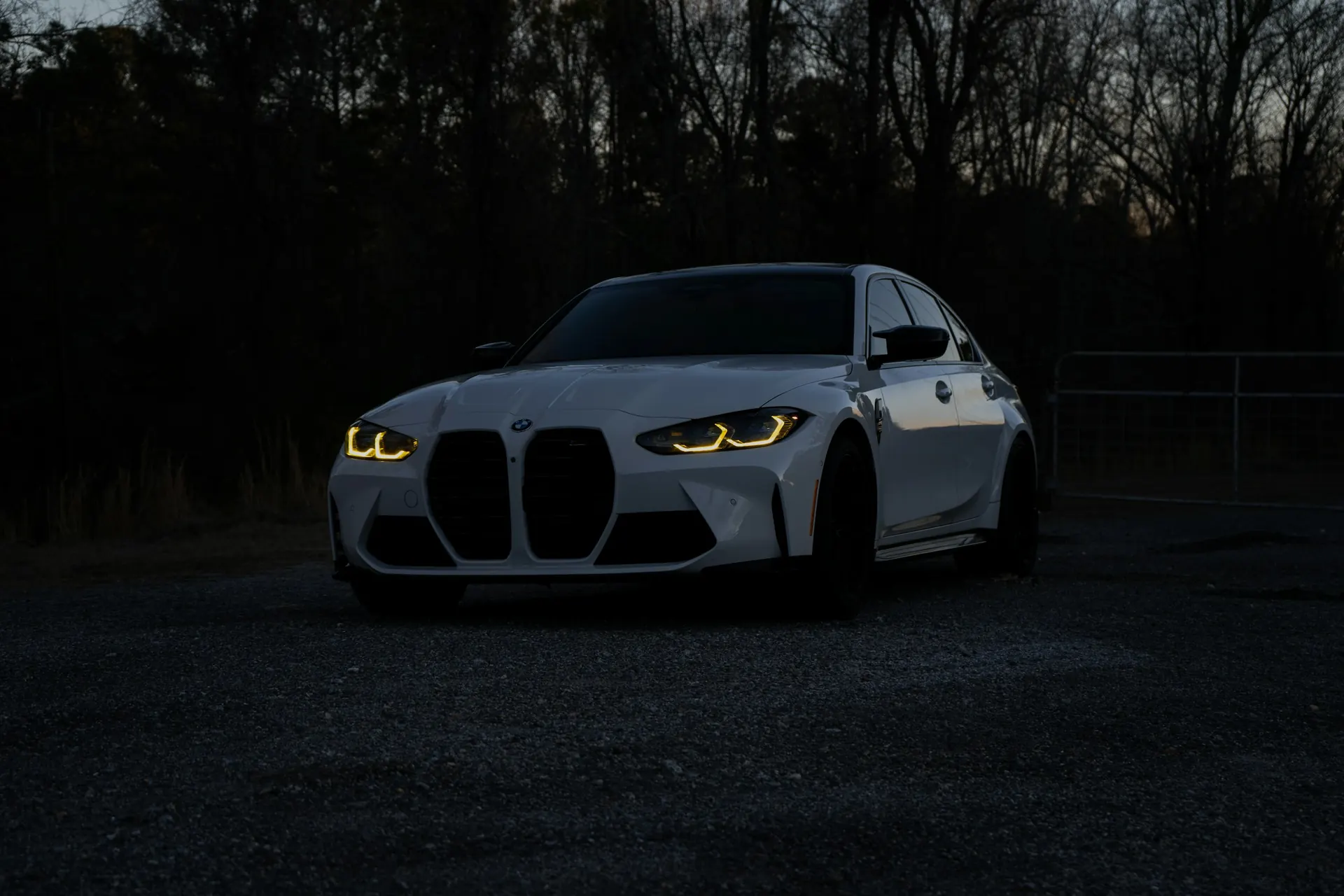 White BMW M3 (G80) with its headlights on at dusk