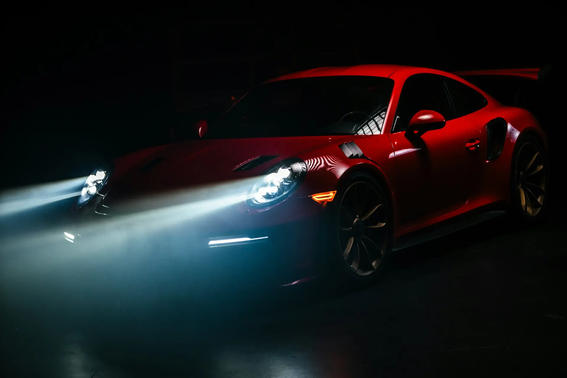 Red Porsche 911 GT3 RS with its headlights on in the dark